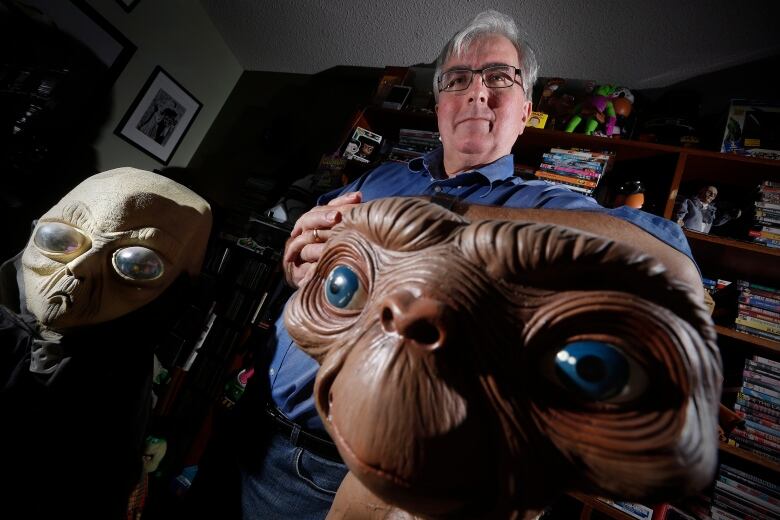 A man stands in front of two figurines of aliens.