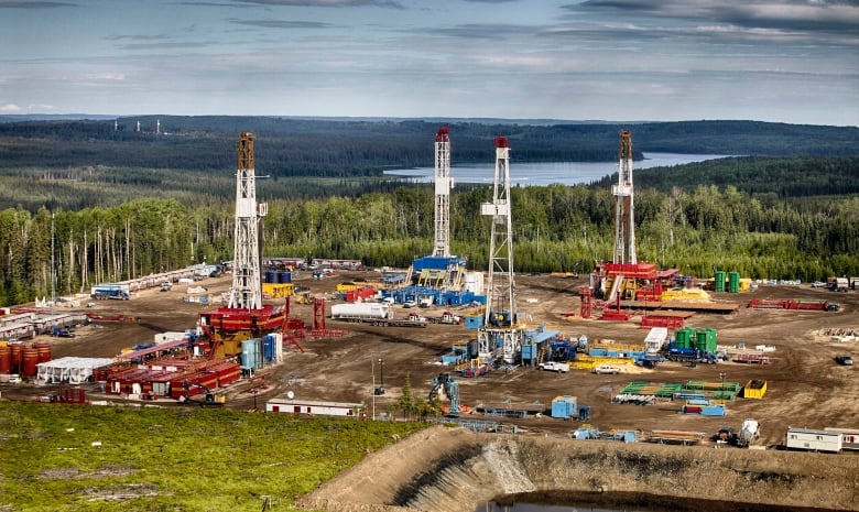 An aerial view of a drilling operation with forests and a lake in the distance.