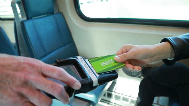 A transit rider taps a Presto card on a fare inspection reader.