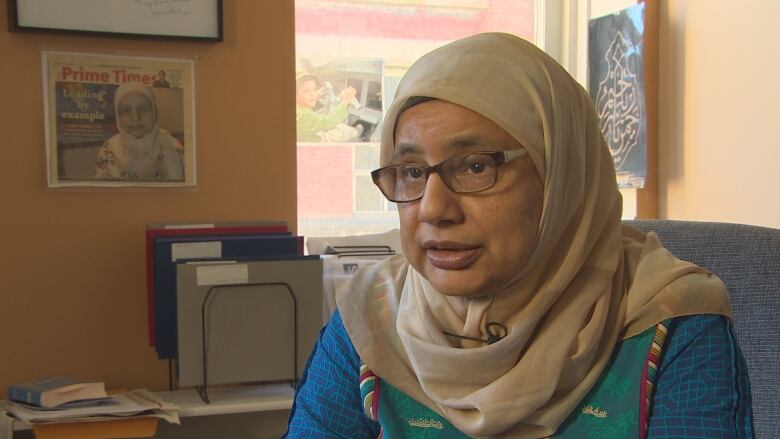 A woman wearing a beige-coloured hijab is seated on a chair.