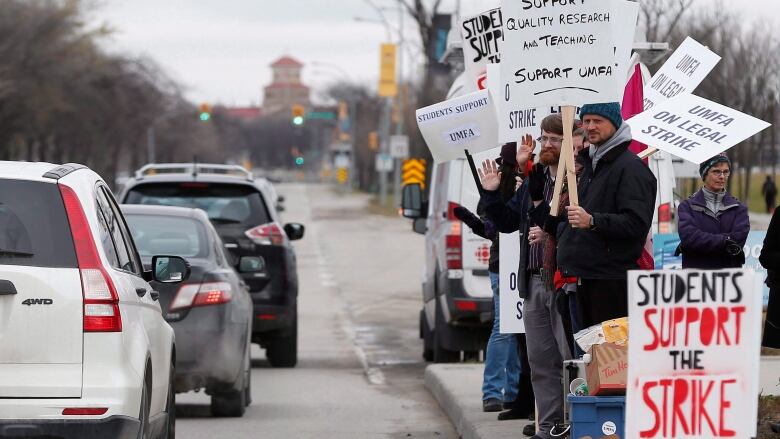 Strikers hold picket signs as cars drive by.