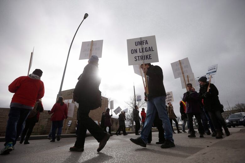 People walk in front of a building holding signs.