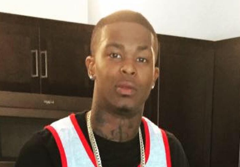 A Black man wearing a red, white and black t-shirt and a gold chain