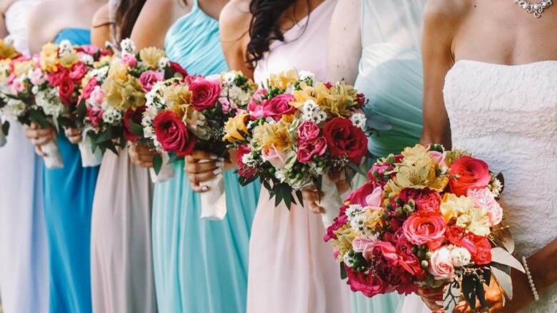 A bride and bridesmaids are seen in a row in this close-cropped photo showing the bodices of their gowns as well as matching flower bouquets.