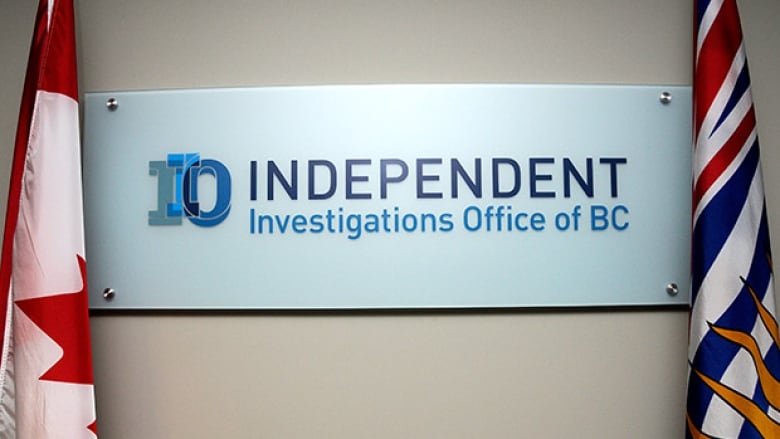 A white sign, framed by the Canadian flag and British Columbia provincial flag. The sign shows the Independent Investigations Office of B.C. logo and name.