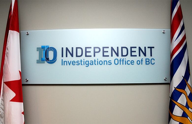 A white sign, framed by the Canadian flag and British Columbia provincial flag. The sign shows the Independent Investigations Office of B.C. logo and name.