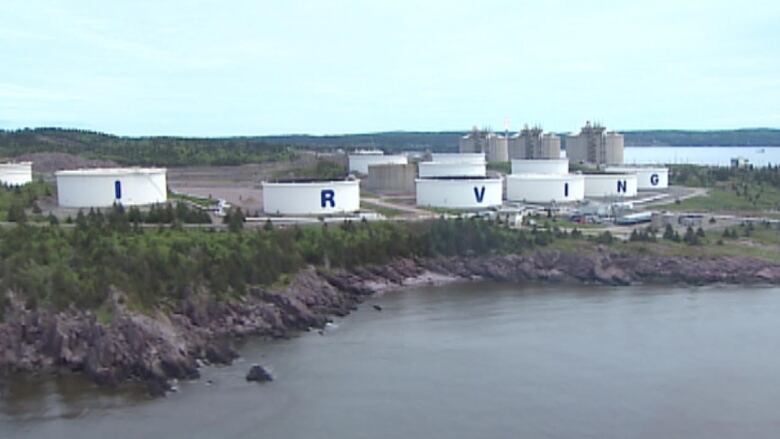 A piece of land next to the water with big tanks along the edge, each with a letter on them, spelling out IRVING