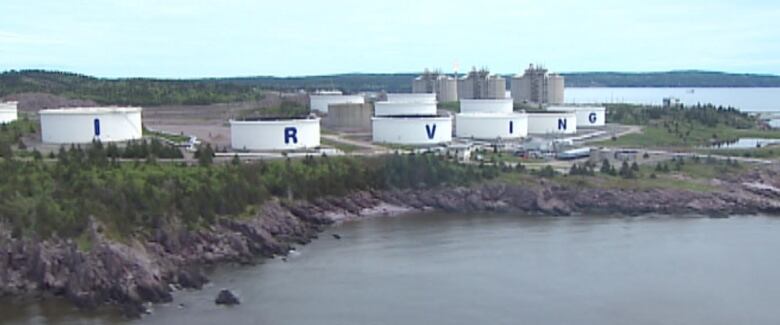 A piece of land next to the water with big tanks along the edge, each with a letter on them, spelling out IRVING