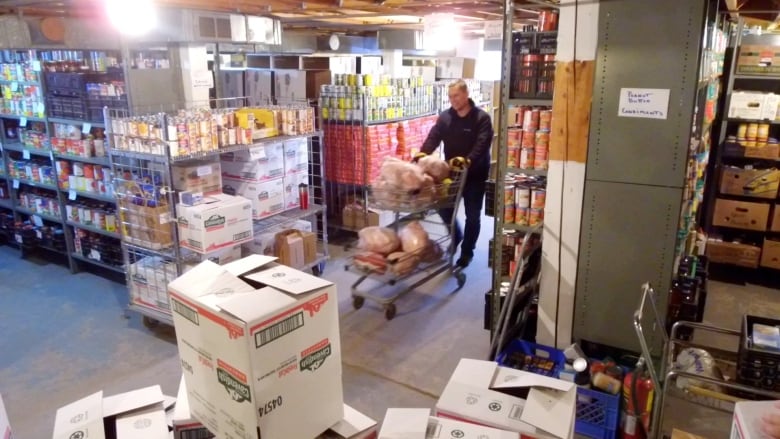 A man wheels a shopping cart of turkeys to the freezers in a warehouse room full of food.