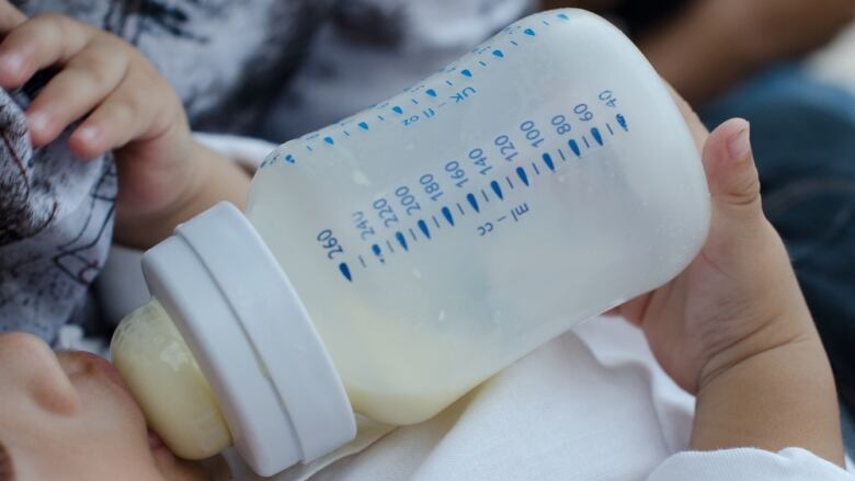 A closeup of a baby drinking formula from a bottle.