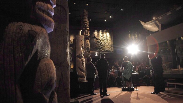 People stand on a stage among totem poles