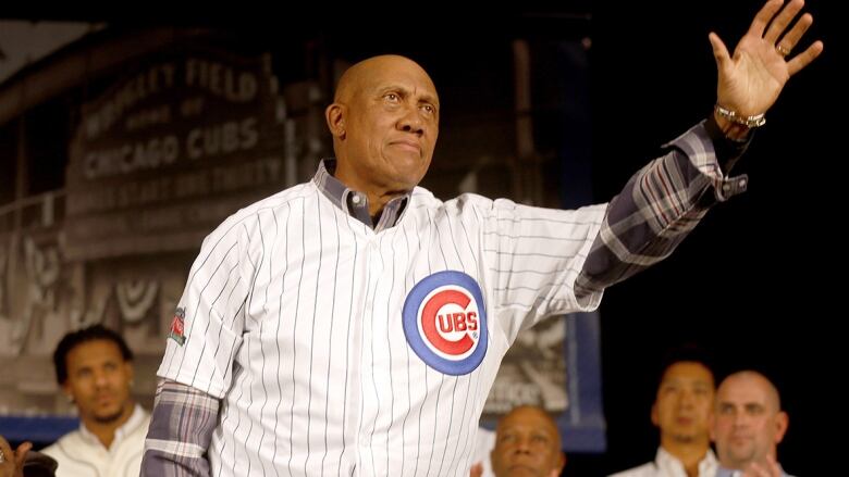 A man wearing a Cubs jersey overtop of a flannel shirt waves to an unseen crowd.