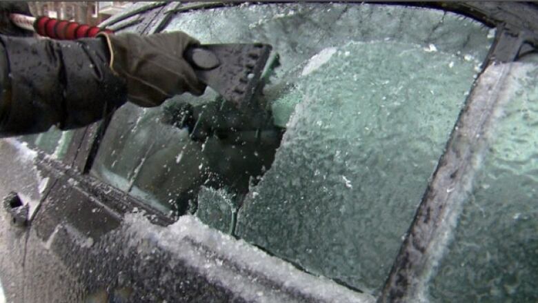 An icy car window with someone using a car scraper to remove the ice