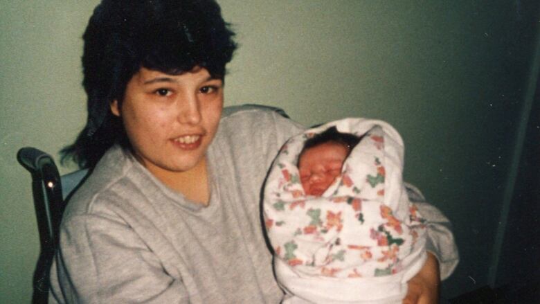 A woman sits in a chair holding a small child. 