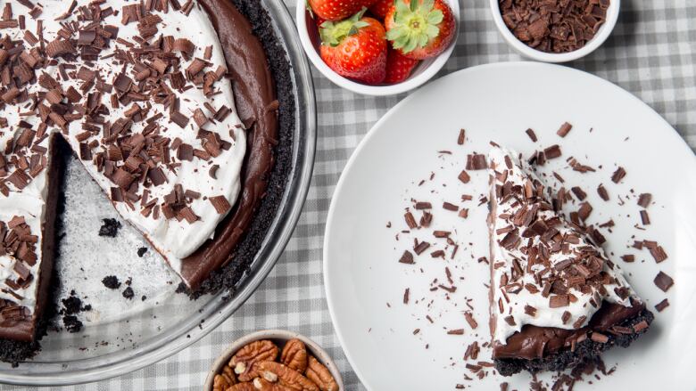 Overhead shot of a chocolate mud pie with a slice of it on a white plate on a table. 