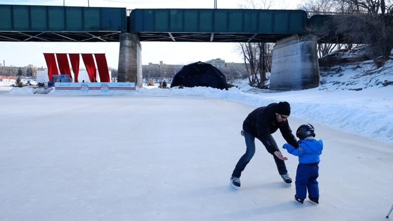 A man holding reaching out for a child. Both are skating on a frozen river.