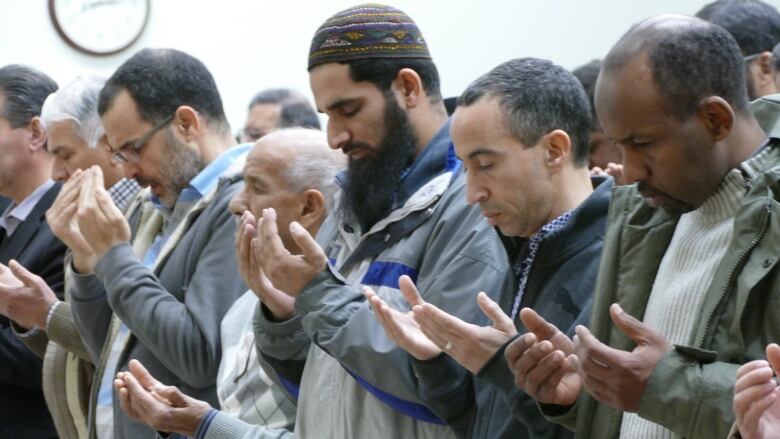 A group of men bow their heads and raise their hands as they pray.