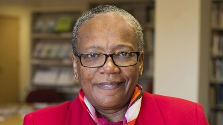 A Black woman with short hair is seen wearing glasses and a red blazer