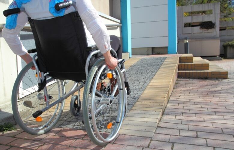 From behind, we see a person in a wheelchair going up a wheelchair ramp.