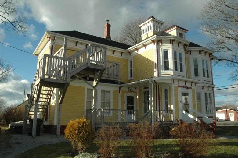 A yellow and white 7-bedroom house with a large wooden staircase on the side. 