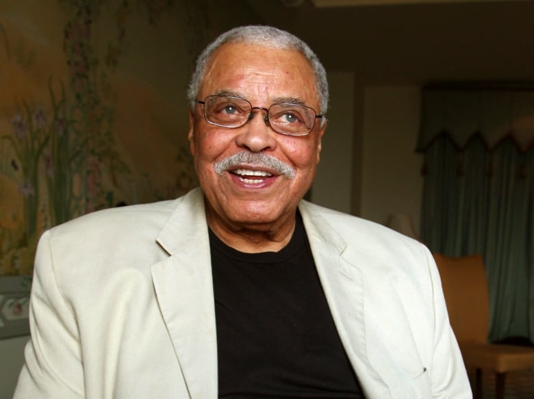 A man in a white suit with a black shirt underneath smiles at the camera.