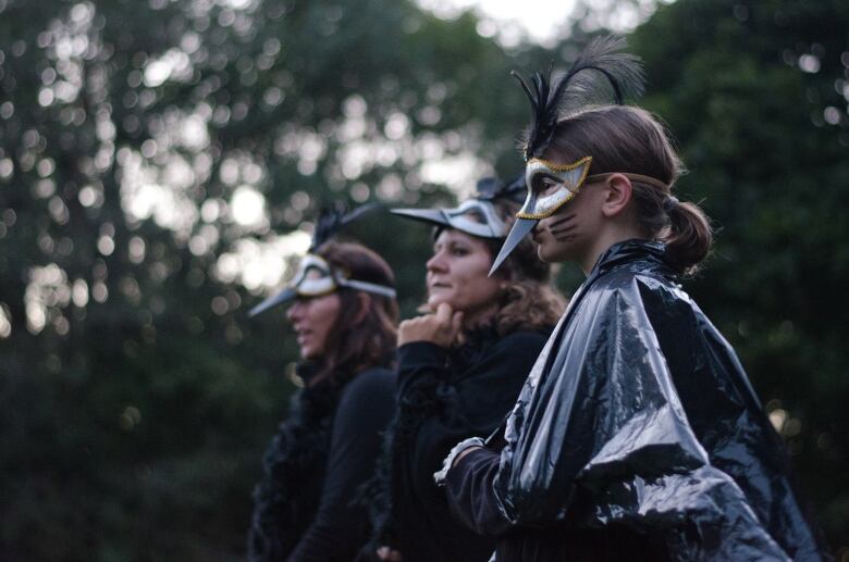 Three women are dressed in black and crow masks.