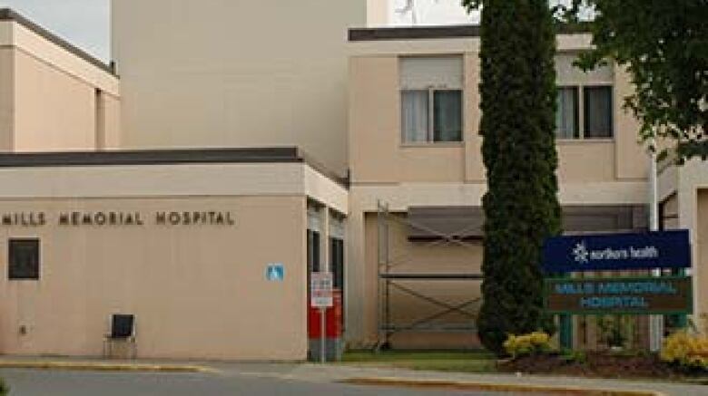 A small hospital patient drop-off area with a tree and sign.