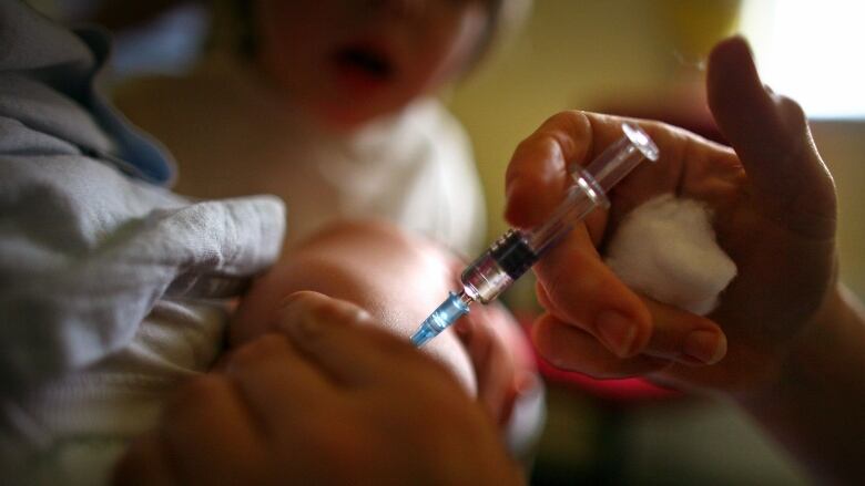 A close up of a hand giving a vaccine to a baby. 