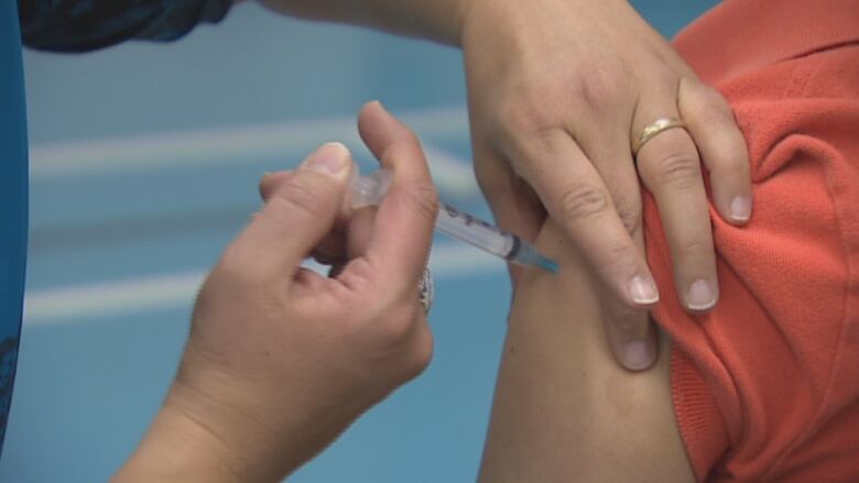 A person injects another person with a syringe on their upper arm.