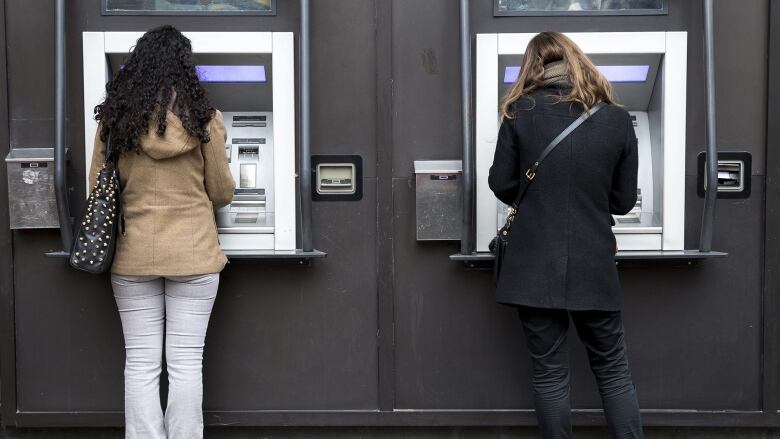 Two women use ATM banking machines in Toronto.