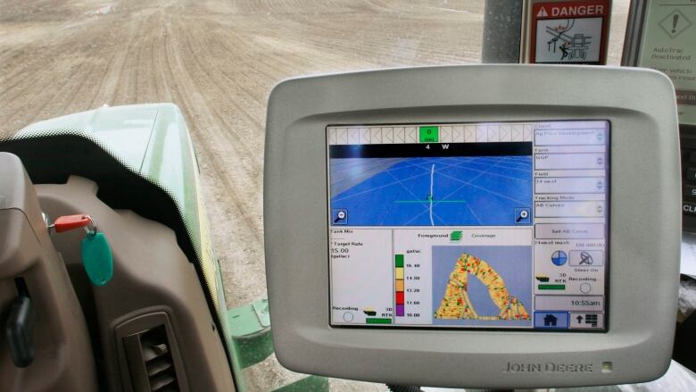 A computer monitor is seen inside a tractor cab with a farm field in the background.