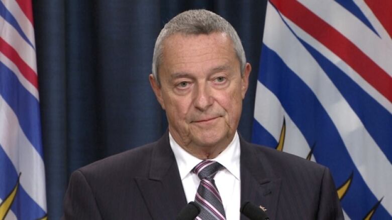 A man at a podium with flags behind.