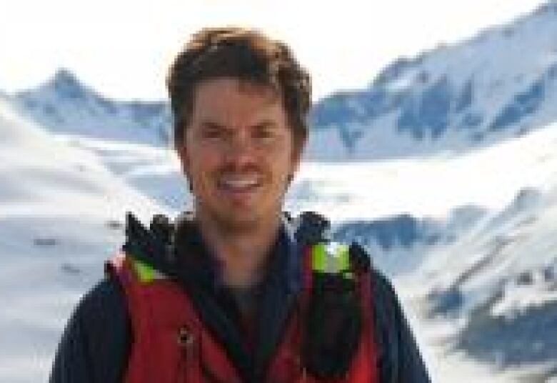 A man in a hi-vis jacket stands in front of a mountain. 