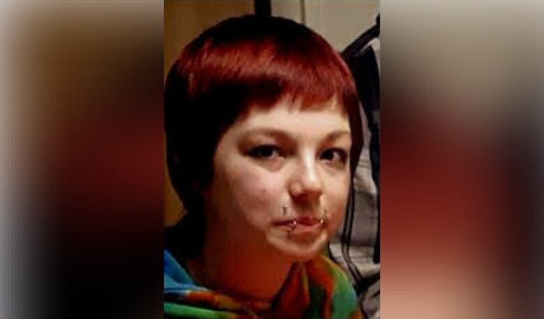 A teenaged girl with short, dyed red hair and several face piercings. 