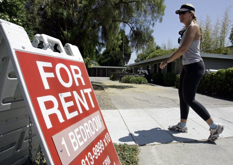 A woman walks past a 'For Rent' sign.