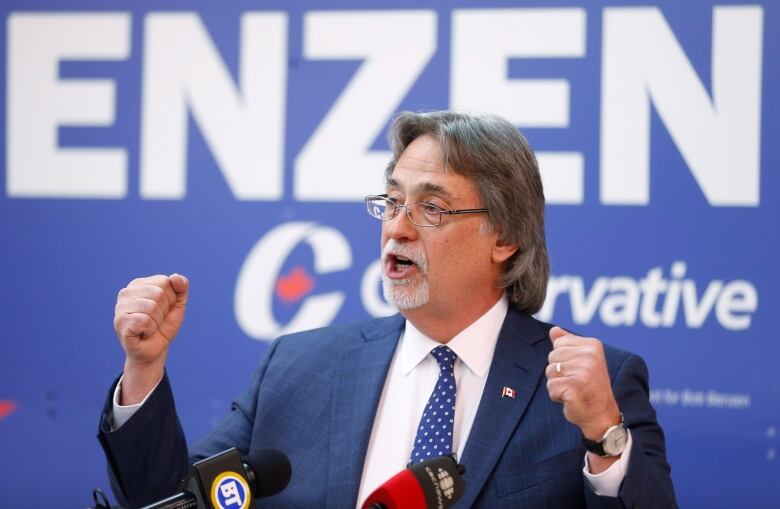 A man shakes his fists in front of a blue sign. 