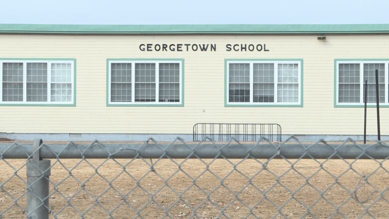 A long, one-story cream-coloured building is visible behind a fence, with the words 