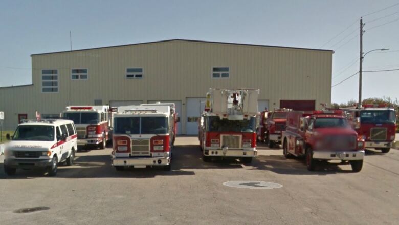 Six fire trucks are see in front of a large beige building.