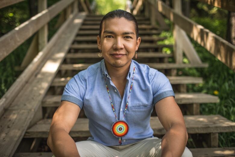 Dr. James Makokis sits on wooden stairs outside.