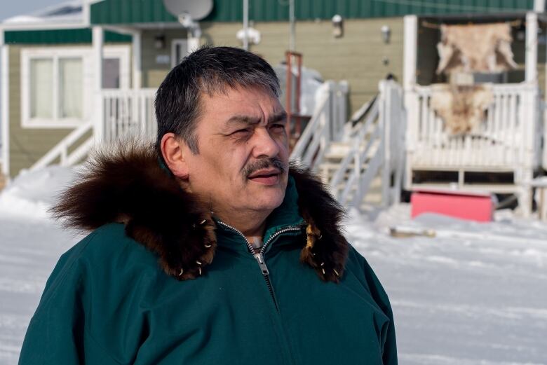 A man wearing a parka stands outdoors in winter.