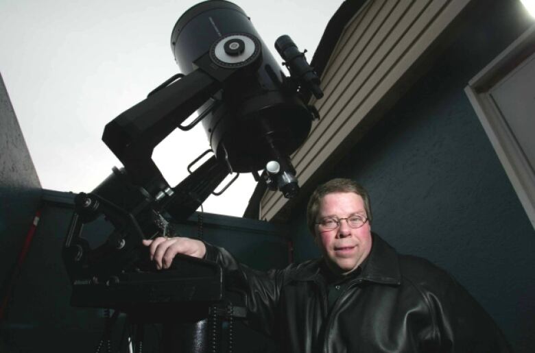 A man stands behind  a telescope