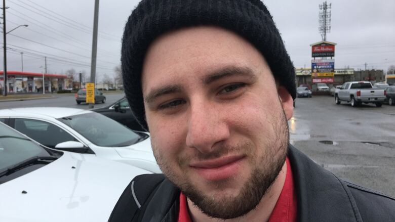 A young man standing in a parking lot, wearing a black toque.