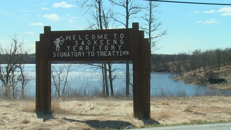 A wooden sign is pictured near a lake. It says, 