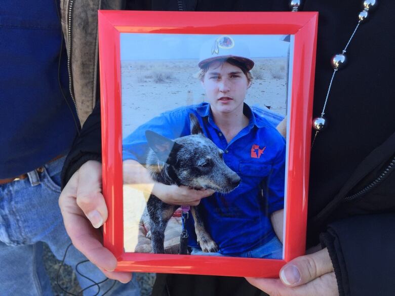 A hand hold a framed photograph of a young boy with his dog. 