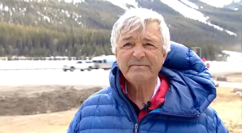 A man stands in front of a mountain. 