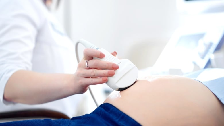 An arm using an ultrasound wand on a person's pregnant belly.