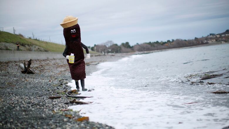 A person in a costume that looks like a cartoon piece of feces walks in the ocean.