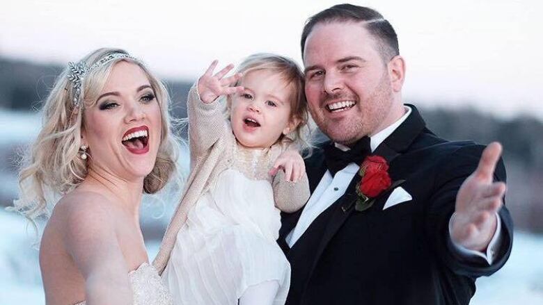 A couple dressed for a wedding hold a young girl in their arms 