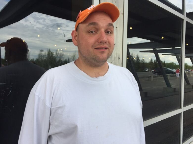 A man in a white t-shirt with an orange baseball cap.