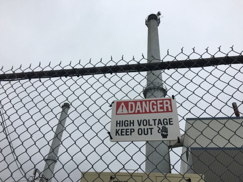 Two smokestacks behind a fence with a sign that says: 